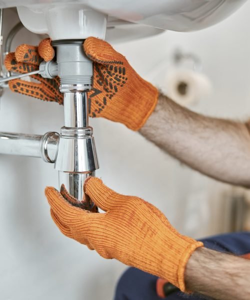 Close up of young man in work gloves repairing silver stainless steel drain pipe